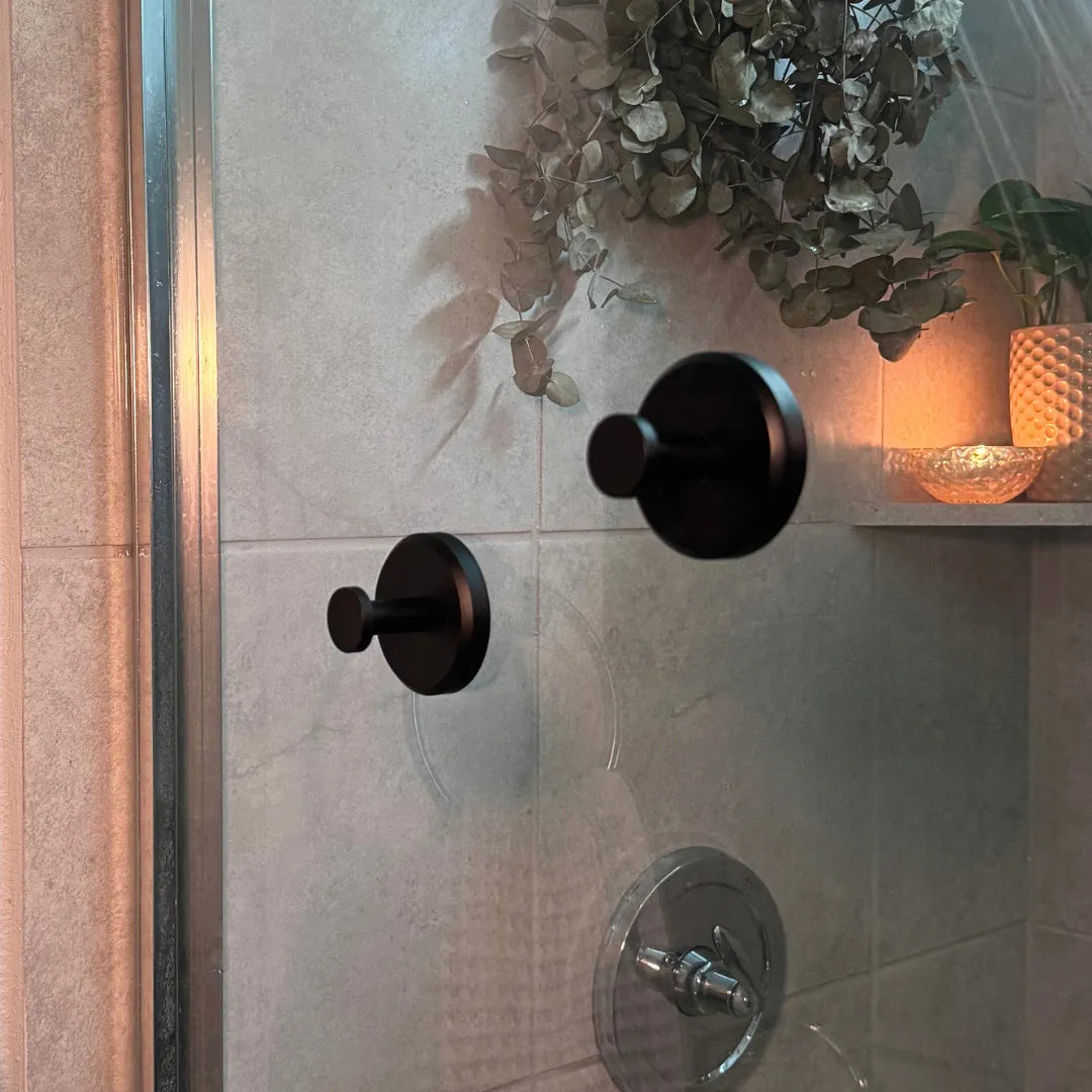 Élégants crochets ventouse noirs fixés sur une surface vitrée d'une salle de bain