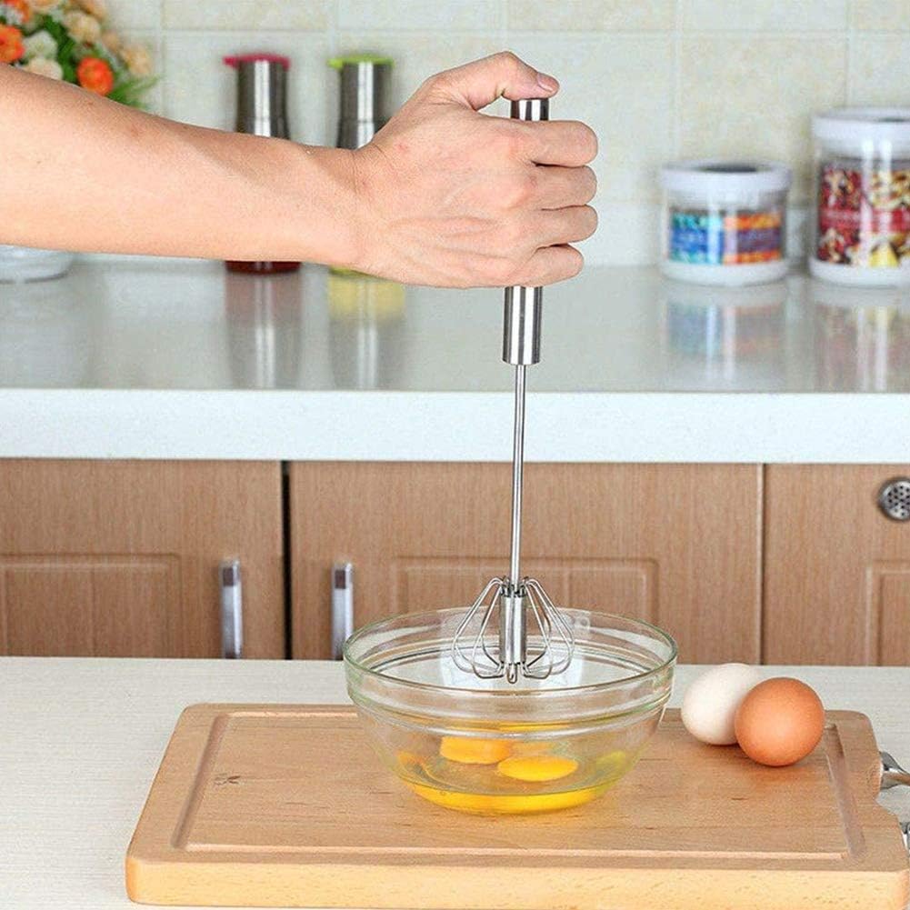 Une main tient un fouet en inox rotatif prêt à battre deux œufs dans un saladier en verre