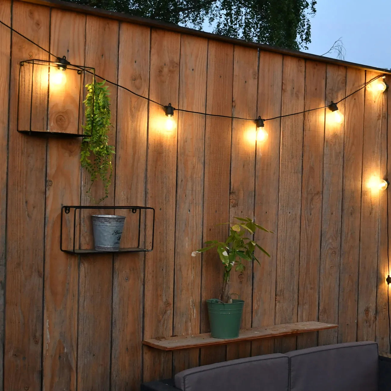 Une guirlande solaire décore une palissade en bois dans un jardin au crépuscule