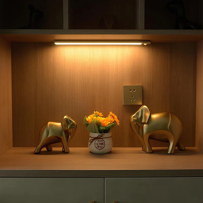 Une lampe aux leds avec un éclairage doux éclaire deux statuettes en forme d'éléphant dans un meuble