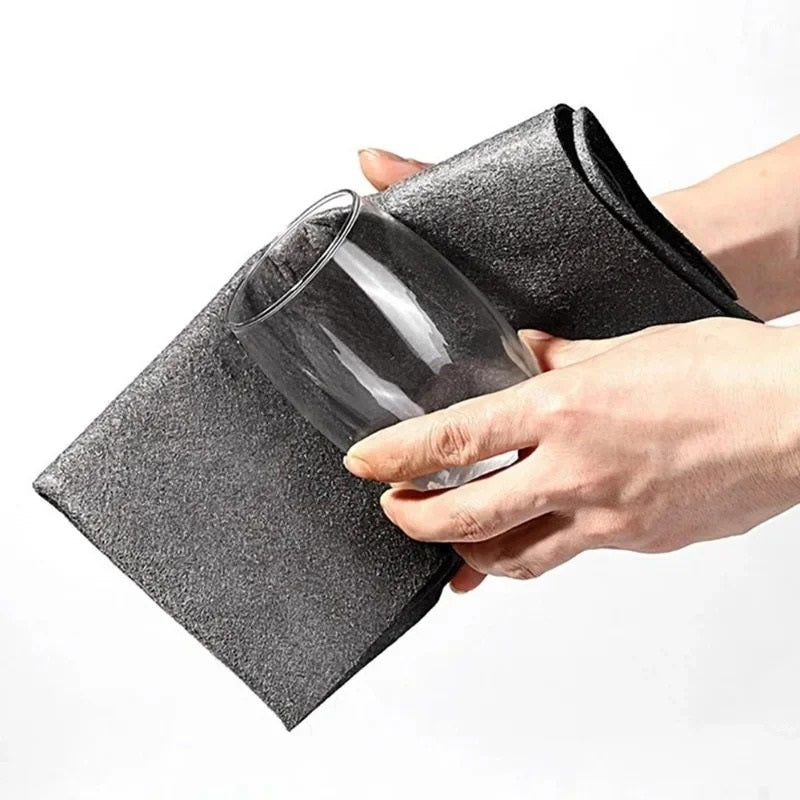 Des mains utilisent un chiffon magique noir pour faire briller sans traces un verre de table