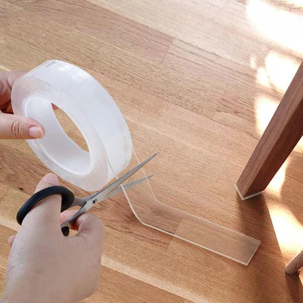 Une main munie d'une paire de ciseaux découpe un ruban fixation extrême pour coller un objet sur le sol en parquet de bois