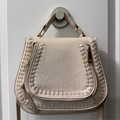 Un crochet design maintient un lourd sac à main en cuir contre un mur clair
