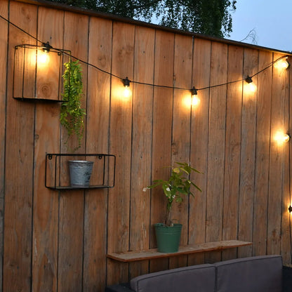 Une guirlande solaire décore une palissade en bois dans un jardin au crépuscule